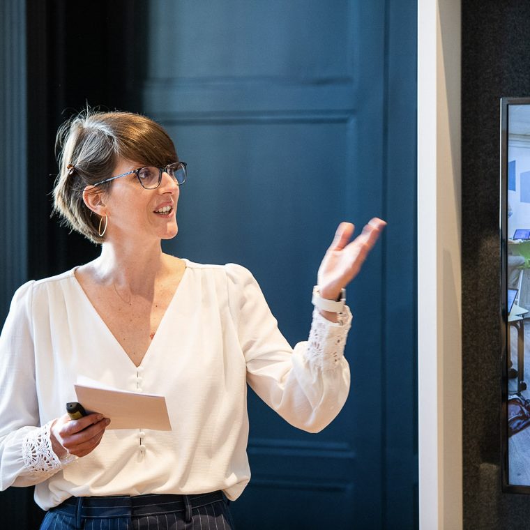 Femme souriante avec des lunettes, portant un haut noir, les bras croisés : Sarah Lachise, votre coach